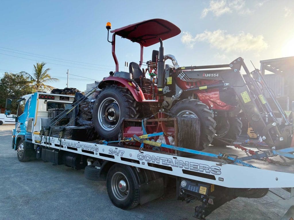 Darren’s Towing tow truck towing a new red tractor in Townsville.